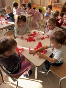 grupa dzieci siedząca przy stoliku bawiąca się czerwona bibułą