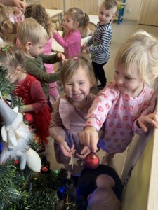 dzieci z uśmiechem ubierają choinkę