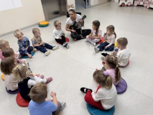 dzieci siedzą w kole, kobieta trzyma ukulele
