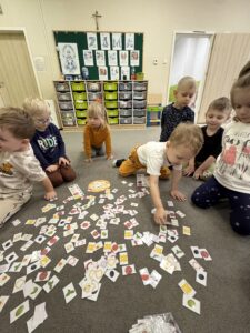 grupa dzieci siedząca na dywanie, w rozsypanymi obrazkami