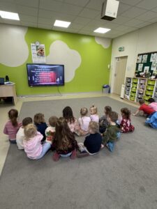 dzieci siedzące na dywanie, oglądające film edukacyjny.