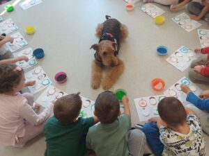 pies leżący na podłodze, wokół kolorowe kubeczki oraz siedzące dzieci