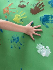 zielona kartka z kolorowymi dłońki i dłonią dziecka