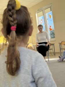 warkocz dziewczynki, w tle widać kobietę czytającą opowiadanie