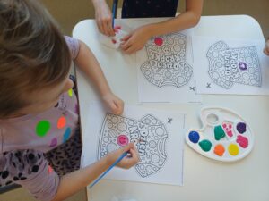 ręce dzieci siedzących przy stoliku wykonujących prace plastyczną