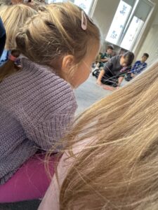 grupa dzieci siedzace na dywanie na środku siedzi dziecko czytające książkę