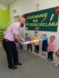 mężczyzna przykładający kredkę na ramię dzieci na znak pasowania